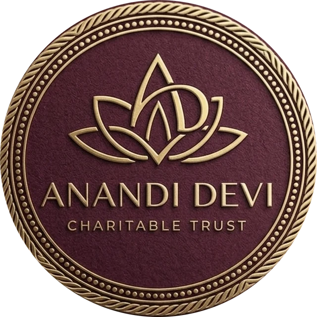 The Anandi Devi Charitable Trust emblem: a lotus enclosing the initials A and D, bordered by a braided golden circle, on deep maroon